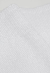 Weißer Textilstoff mit einer gewebten Struktur, der feine Fäden und einen leichten Glanz zeigt, gefaltet, um Tiefe und Dimension darzustellen.