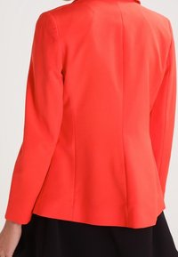 Korallblazer med skräddarsydd design, med långa ärmar, notchad krage och slät textur som framhäver en smal siluett.