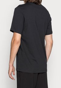 Svart bomulls-T-shirt med kort ärm, rundad halsringning och en enkel design. Slät textur med minimal sömdetalj.