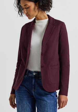 Blazer bourgogne avec deux poches plaquées, coupe ajustée, matière texturée, porté sur un haut blanc en côte et un jean en denim bleu.