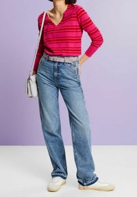 Fuchsia gestreifter Pullover, hellblaue, weit geschnittene Jeans, grauer Gürtel, kombiniert mit weißen Turnschuhen. Schlichte Umhängetasche. Weiche Texturen.