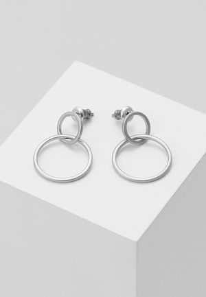 Sølv hoop øreringe med sammenkoblede cirkulære designs. Glat metaloverflade, med en stift bag som sikrer sikker brug. Vist på en hvid podium.