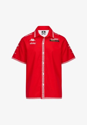 Maglietta rossa a maniche corte con motivo geometrico bianco lungo il colletto e le maniche, con diversi loghi sulla parte anteriore e sui lati.