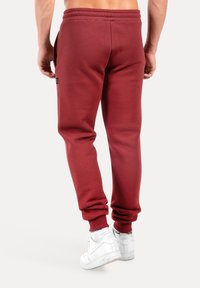 Bordeauxrote Jogginghose mit elastischem Bund und Bündchen, ausgestattet mit Seitentaschen. Kombiniert mit weißen Sneakers für einen lässigen Look.