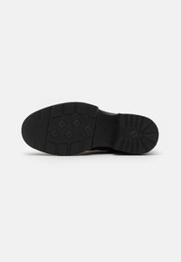 Semelle de chaussure en caoutchouc noir avec grip texturé, présentant une surface à motifs et un profil géométrique pour l'adhérence. Forme plate et arrondie avec un design durable.
