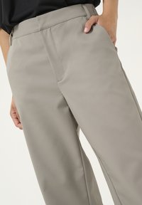 Pantalons ajustés gris clair avec une texture lisse, dotés de poches latérales et d'une taille ajustée, présentés de la hanche vers le bas.