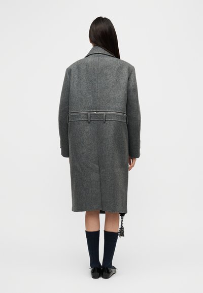 Γκρι μάλλινο παλτό με ζώνη στη μέση, μεγάλο γιακά και κουμπωτά μανίκια. Διαθέτει ευθεία γραμμή και πλαϊνές τσέπες, εμφανιζόμενο από πίσω.