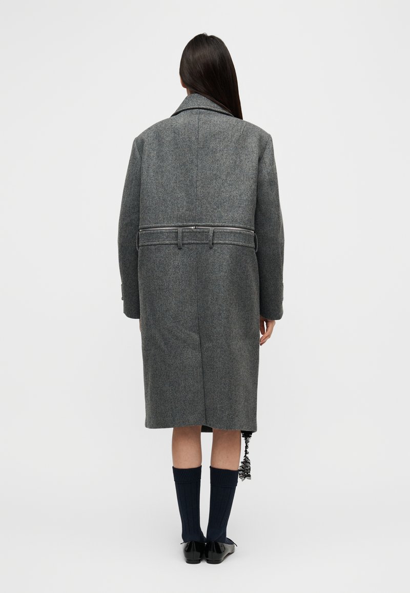 Manteau en laine grise avec ceinture à la taille, grand col et poignets boutonnés. Coupe droite avec poches latérales, présenté de dos.