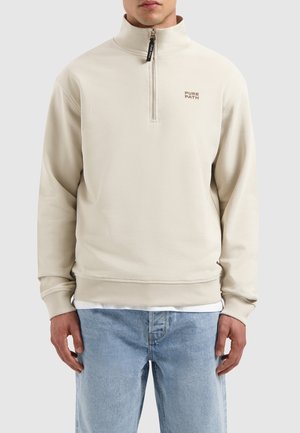 Beige zip-up sweatshirt with high collar, ribbed cuffs and hem, featuring "PURE PATH" logo in brown on the left chest. Soft texture.