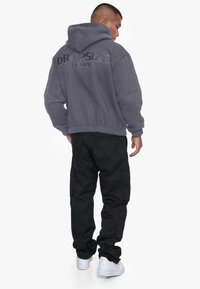 Hanorac gri cu glugă și logo-ul "DROPSIZE EST.2020". Asortat cu pantaloni cargo negri și adidași albi. Material texturat, croială lejeră.