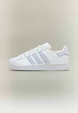 Λευκό παπούτσι Adidas Superstar με ανοιχτό μωβ ρίγες, κορδόνια και σχέδιο με προστασία στο δάκτυλο σε απλό μπεζ φόντο.