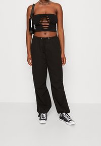Černý bandeau top s výřezem kombinovaný s volnými černými cargo kalhotami, které mají stahovací pas a žebrovanou texturu. Oblečeno s černými vysokými teniskami.