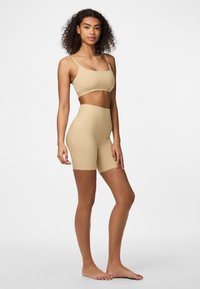Bežový bezšvový crop top a šortky s vysokým pásom, vyrobené z elastického materiálu. Obsahuje tenké ramienka a hladkú, matnú textúru.