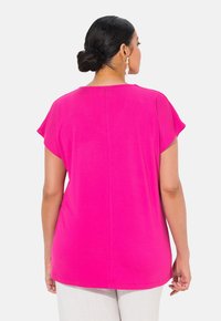 Světle růžový lehký top s krátkými rukávy, zakřiveným výstřihem a uvolněným střihem. Hladká textura a rovný lem viditelné na spodní části.