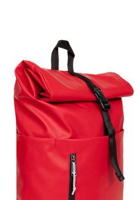 Zaino rosso a roll-top realizzato in materiale impermeabile e liscio, con spallacci neri e una tasca frontale con zip, caratterizzato da una chiusura a fibbia.