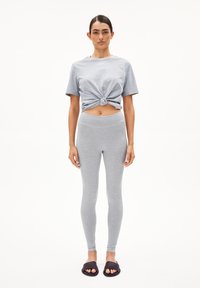 Gray cotton t-shirt with a knotted front, paired with gray leggings. Model wears black slide sandals; minimalist design and smooth texture.