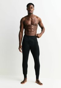 Čierne legíny vyrobené z mäkkej tkaniny, s priliehavým strihom, elastickým pásom a manžetami na členkoch. Detailné prešívanie pozdĺž švov.