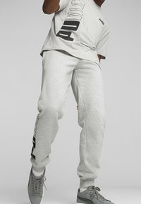 Jasnoszara bawełniana koszulka T-shirt z czarnym logo po boku, w zestawie z dopasowanymi szarymi spodniami dresowymi z bocznymi kieszeniami i elastycznymi mankietami.