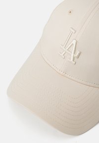 Kappe i lys beige stoff, med teksturert overflate og sydd detaljer. Brodert LA-logo i matchende farge foran.