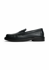 Mocasines de cuero negro con punta redondeada, detalles de costura, un tacón bajo y un acento de tira horizontal en la parte delantera.