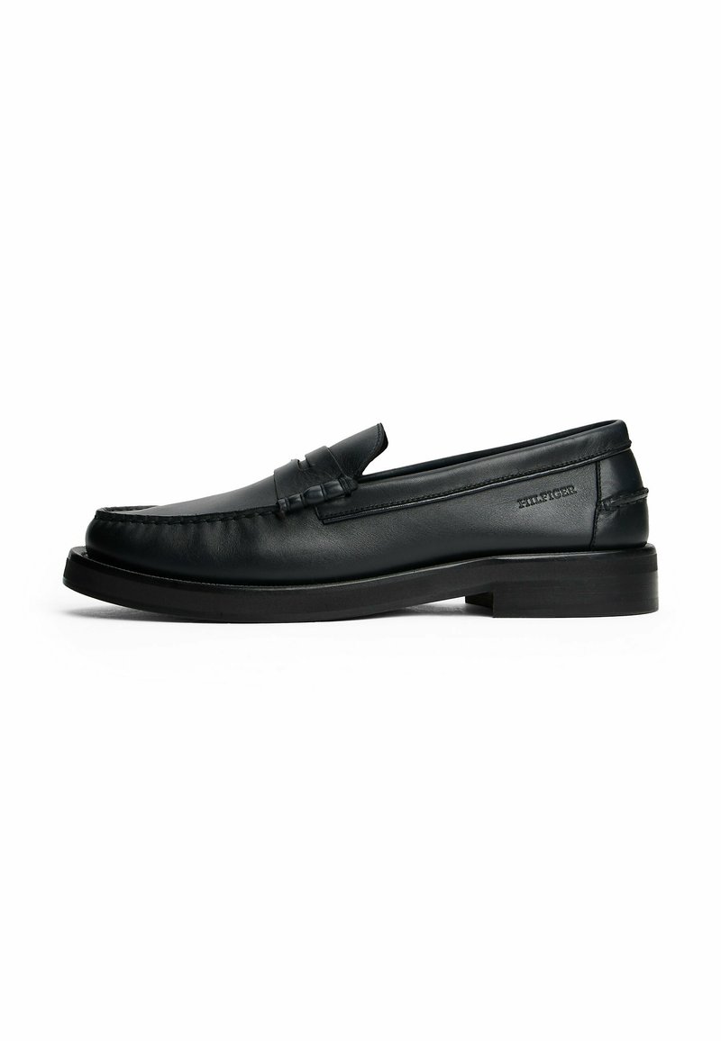 Mocasines de cuero negro con punta redondeada, detalles de costura, un tacón bajo y un acento de tira horizontal en la parte delantera.