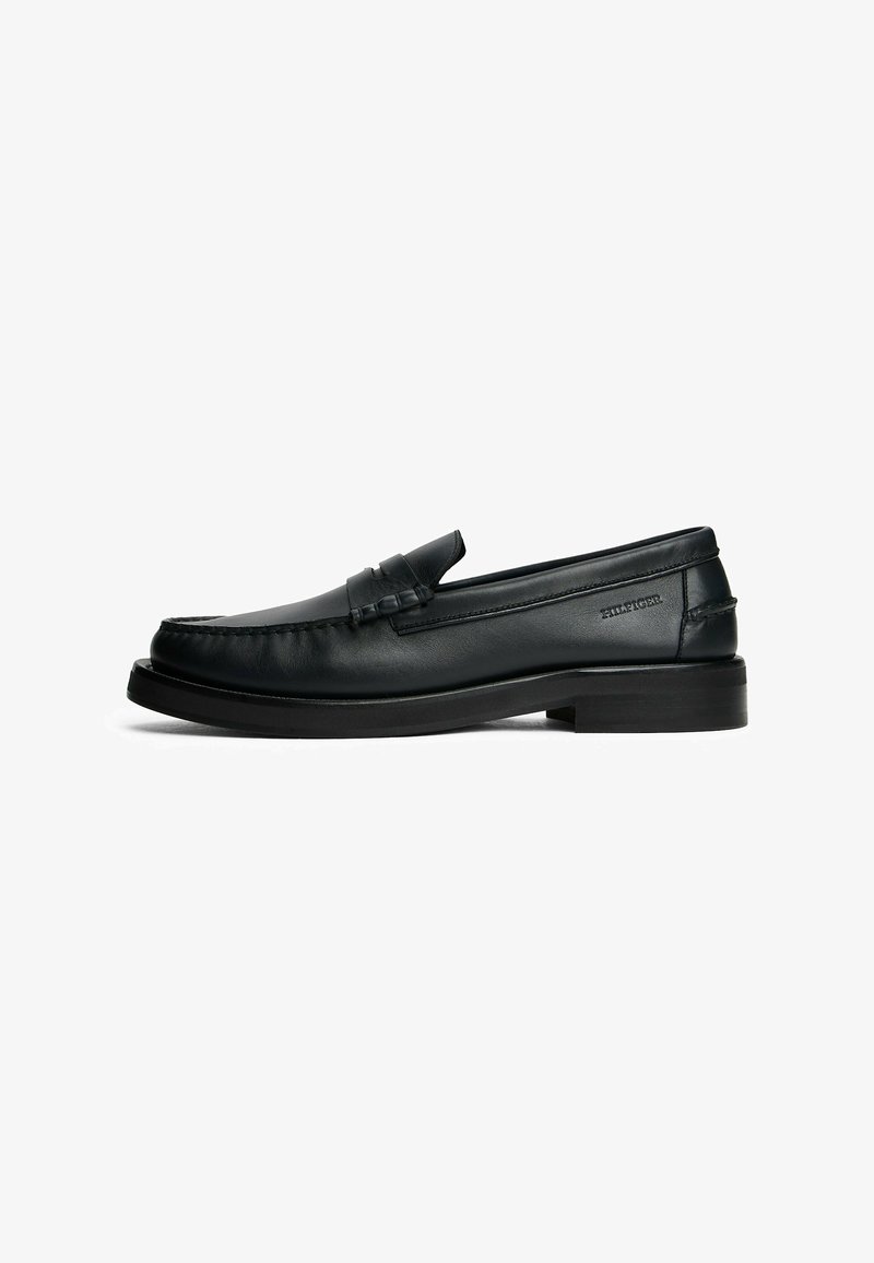Mocasines de cuero negro con punta redondeada, detalles de costura, un tacón bajo y un acento de tira horizontal en la parte delantera.