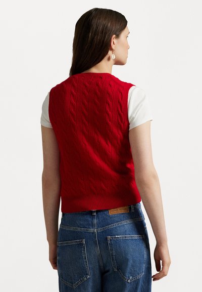 Pulover mânecă scurtă, tricotat în model cu cabluri, de culoare roșie, cu tiv ondulat, purtat peste o cămașă albă, asociat cu blugi denim albaștri, cu talie înaltă.
