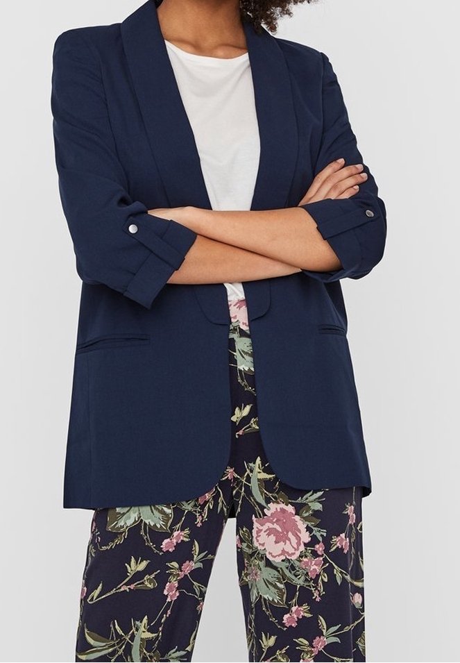 Mörkblå kavaj med sjalkrage, enknappsstängning och uppvikta ärmar, i kombination med blommönstrade byxor med pinka och gröna motiv.