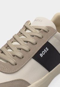 Μπεζ και κρεμ αθλητικό παπούτσι με υφασμένα κορδόνια και μαύρο πλαϊνό πάνελ με λευκό λογότυπο "BOSS", κοντινή λήψη στην πάνω και περιοχή κορδονιών.