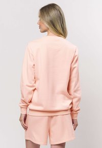 Broskvová mikina s dlouhými rukávy a žebrovanými manžetami, v kombinaci s odpovídajícími šortkami; hladká látka s volným střihem.