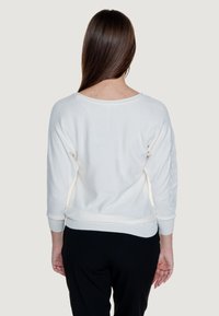 Maglione bianco con scollo ampio e maniche a tre quarti. Presenta lettering testurizzato "GUESS" sulla manica sinistra. Tessuto a maglia morbido.