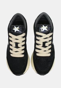 Baskets en suede noir avec des lacets crème, présentant un dessus texturé, une semelle en caoutchouc blanc et un logo décoratif sur la languette avec un détail en étoile.