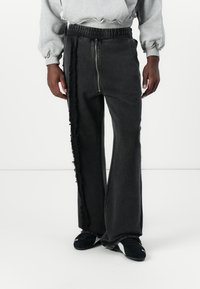 Sorte denimbukser med en flagrende design, der har en sidelukning, slidte sømme og elastisk talje. Fremhævet med en falmet tekstur.