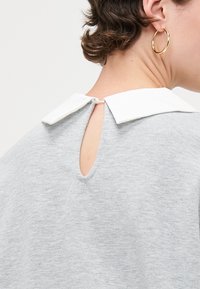 Grauer Pullover mit weißem Kragen, Rückendetail mit Schlitz, weicher Stoffstruktur und gerundetem Ausschnitt. Hat eine lockere Passform und dezente Nähte.