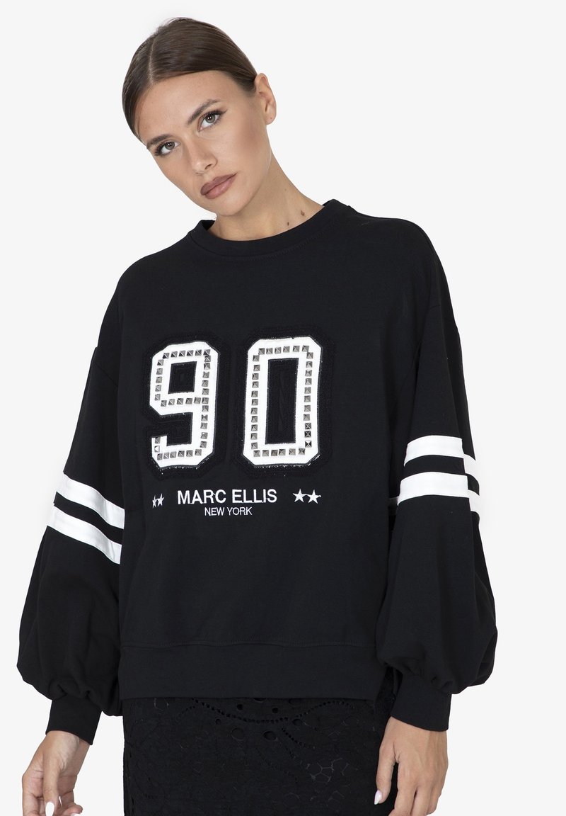 Felpa nera con maniche oversize, caratterizzata da un '90' bianco impreziosito da borchie e 'MARC ELLIS NEW YORK' ricamato in bianco.