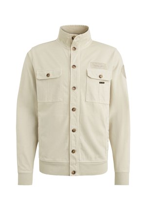 Veste beige avec un col haut, deux poches avant et des boutons marron. Présente des poignets côtelés et un patch en tissu sur le côté supérieur gauche.