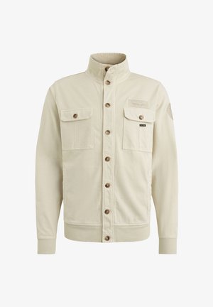 Giacca beige con colletto alto, due tasche frontali e bottoni marroni. Presenta polsini a coste e una toppa di stoffa sul lato sinistro superiore.