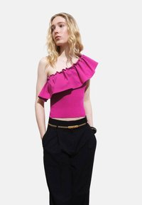 Fuchsia Ein-Schulter-Oberteil mit gerafftem Ausschnitt und geripptem Stoff, kombiniert mit hochgeschnittenen schwarzen Hosen und einem goldenen Kettengürtel.