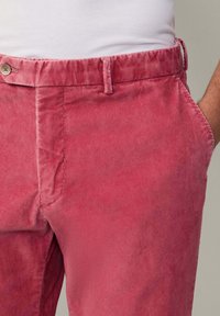 Pantalons en velours côtelé rose avec un motif côtelé texturé, dotés d'une fermeture à bouton et de poches latérales. La ceinture est élastique pour le confort.