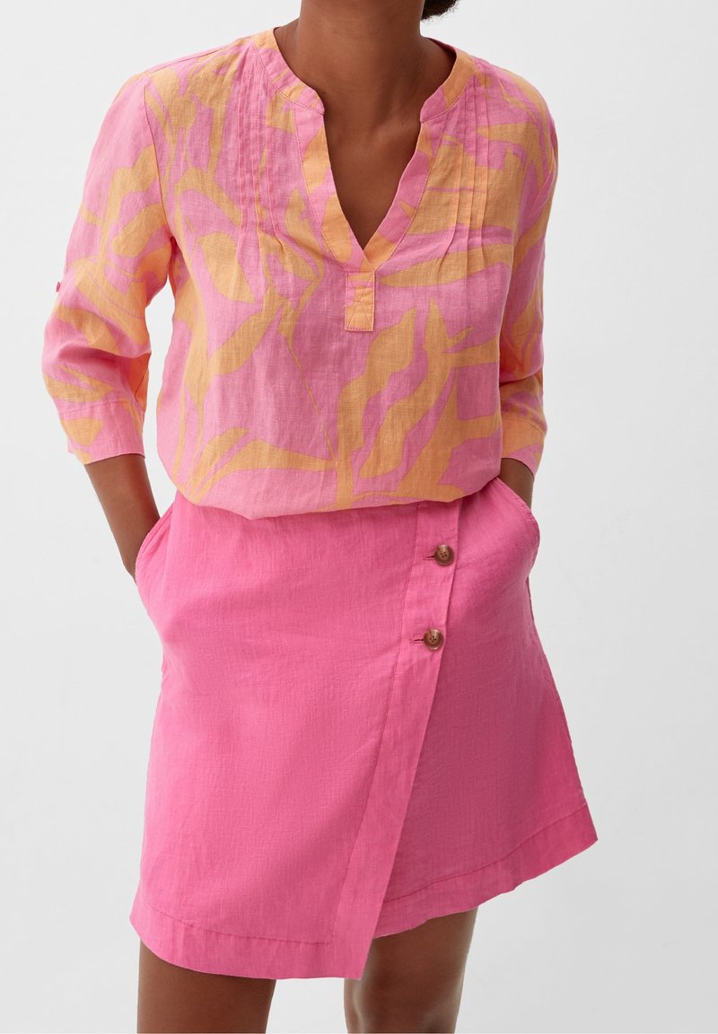 Blouse en lin rose avec un motif ondulé jaune, col en V et manches trois-quarts, associée à une jupe portefeuille en lin rose avec des accents de boutons.