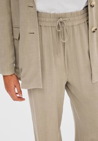 Béžový lehký látkový outfit s elastickým pasem a šňůrkou; doplněný volně střiženým blejzrem s knoflíkovými detaily.