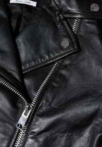 Gros plan sur une veste en cuir noire montrant une fermeture éclair argentée, des boutons-pression et un matériau en cuir texturé.