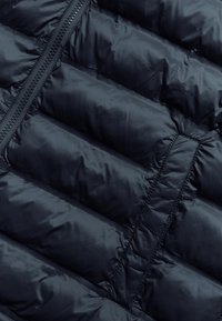 Navy Puffer-Jacke mit gestepptem Muster, horizontalen Nähten und einem Reißverschluss. Das Material wirkt glatt und leicht glänzend.