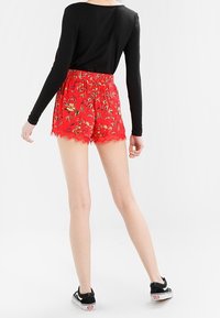 Shorts rossi floreali con orlo sfilacciato, vita elastica e top a maniche lunghe nero. Il modello indossa scarpe nere con dettagli bianchi.