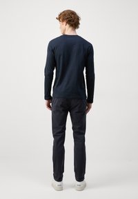 Mørkeblå langærmet skjorte med rund hals, parret med mørke slim-fit bukser og hvide sneakers, set fra ryggen.