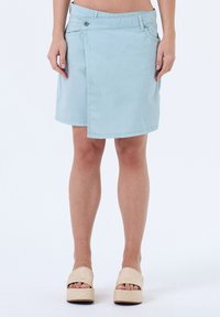 Jupe-culotte en denim bleu clair avec une fermeture à boutons à l'avant. Présente une texture lisse et un ourlet droit, associée à des chaussures compensées en espadrille neutres.