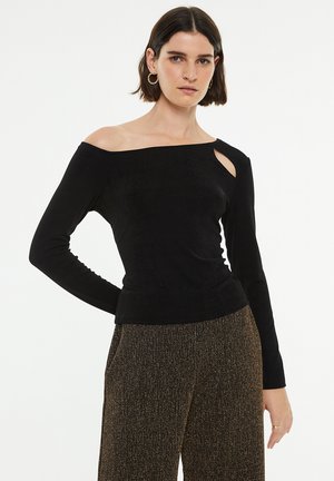 Top negro de manga larga con diseño de hombros al descubierto y un corte lateral, hecho de una tela suave, combinado con pantalones texturizados en dorado y negro.