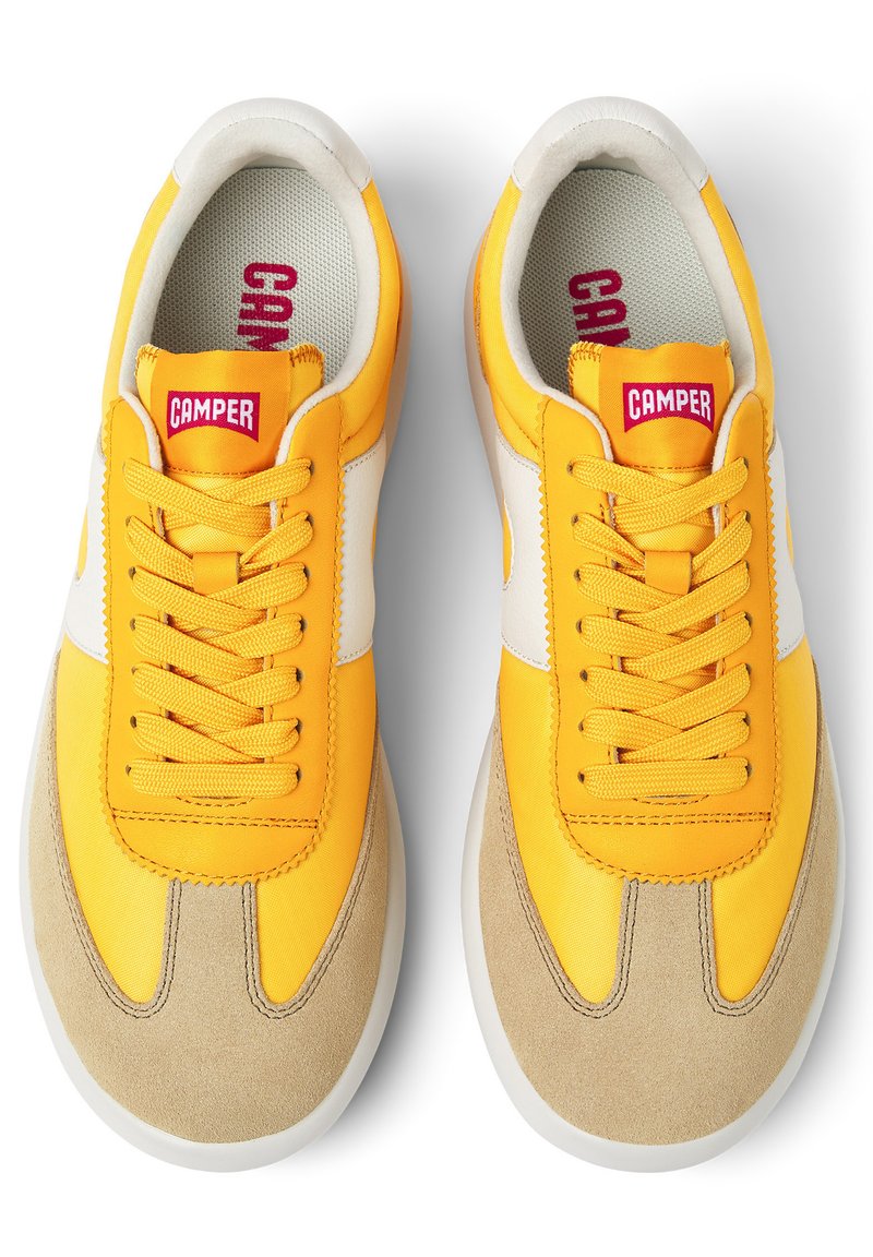 Zapatillas de ante y textil amarillas con raya lateral blanca, puntera redondeada y cordones planos. Presenta una etiqueta roja "CAMPER" en la lengüeta.