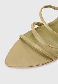 Sandale en satin vert à lanières avec un bout pointu, présentant des fines lanières entrecroisées et une texture lisse et mate sur la semelle.