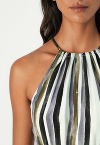 Zöld, fekete, szürke és fehér függőleges csíkos halter top. Az anyag könnyűnek tűnik, összegyűrt nyakkivágással és vékony pántokkal.
